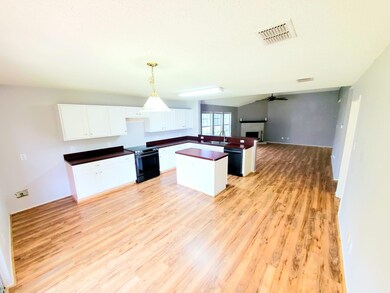Kitchen with black range with electric stovetop, sink, white cabinetry, light hardwood / wood-style flooring, and decorative light fixtures