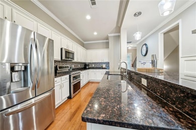 Kitchen with appliances with stainless steel finishes, a sink, white cabinetry, ornamental molding, and backsplash