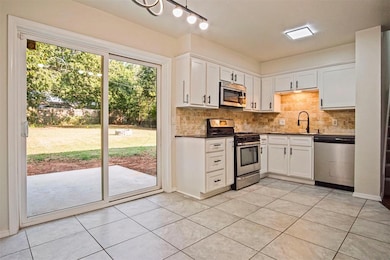 Kitchen featuring appliances with stainless steel finishes, white cabinetry, tasteful backsplash, and light tile patterned floors
