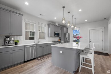 Kitchen with gray cabinets, appliances with stainless steel finishes, light wood-style flooring, backsplash, and recessed lighting