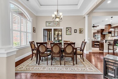 Dining room with ornate columns, dark wood finished floors, ornamental molding, a chandelier, and a tray ceiling