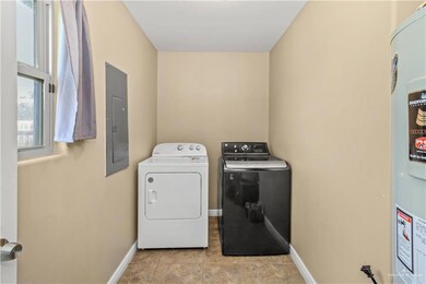 Laundry room with washing machine and clothes dryer, light tile floors, and electric water heater