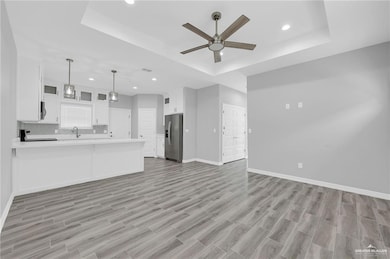 Kitchen with appliances with stainless steel finishes, open floor plan, a raised ceiling, ceiling fan, and a peninsula
