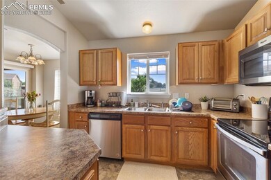 Kitchen featuring appliances with stainless steel finishes, a chandelier, arched walkways, and brown cabinetry