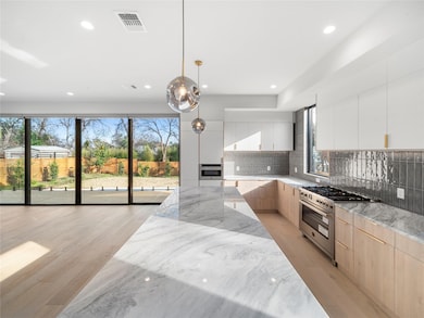 Kitchen featuring modern cabinets, light stone counters, light wood finished floors, appliances with stainless steel finishes, and decorative light fixtures
