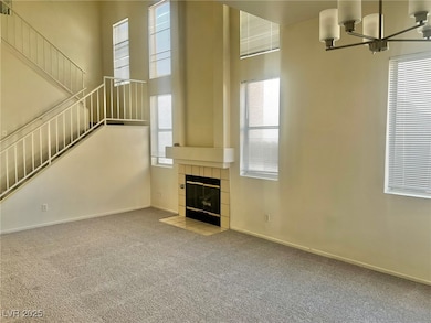 Unfurnished living room with a high ceiling, carpet floors, a tiled fireplace, and a chandelier
