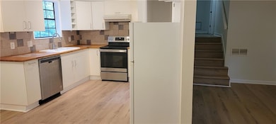 Kitchen with appliances with stainless steel finishes, under cabinet range hood, light wood-style flooring, and white cabinets