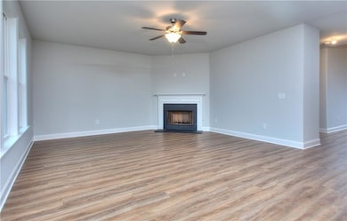 Unfurnished living room featuring light wood finished floors, a fireplace with raised hearth, and ceiling fan