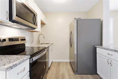 Kitchen featuring stainless steel appliances, white cabinetry, light wood-style floors, and light stone counters