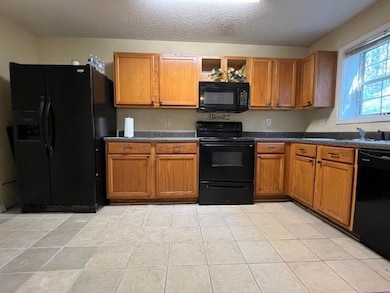 Kitchen with black appliances, dark countertops, brown cabinetry, open shelves, and a textured ceiling