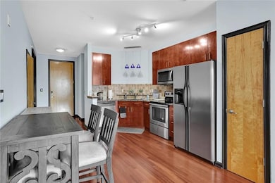 Kitchen with stainless steel appliances, light wood-style floors, backsplash, a sink, and brown cabinets