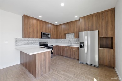 Kitchen with modern cabinets, appliances with stainless steel finishes, brown cabinets, decorative backsplash, and a peninsula