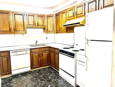 Kitchen featuring white appliances, under cabinet range hood, dark marble finish floors, light countertops, and brown cabinets
