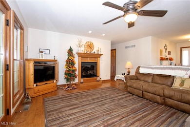 Living room with light wood-type flooring, ceiling fan, and a glass covered fireplace