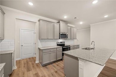 Kitchen featuring gray cabinetry, appliances with stainless steel finishes, backsplash, ornamental molding, and light stone counters