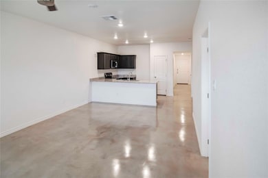 Kitchen with concrete flooring, a peninsula, light stone countertops, stainless steel appliances, and recessed lighting