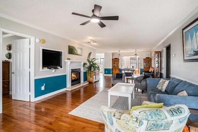 Living area with a textured ceiling, crown molding, wood finished floors, a lit fireplace, and a ceiling fan