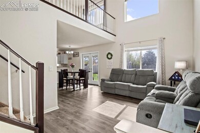Living room with stairs, wood finished floors, a chandelier, a high ceiling, and baseboards