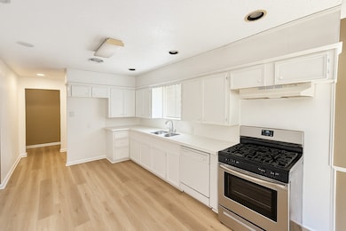 Kitchen featuring stainless steel gas stove, light countertops, dishwasher, white cabinets, and light wood-type flooring