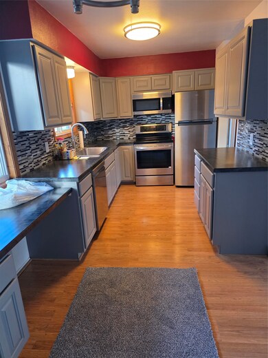 Kitchen with dark countertops, decorative backsplash, appliances with stainless steel finishes, and light wood-style flooring