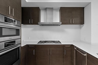 Kitchen with stainless steel appliances, wall chimney exhaust hood, dark brown cabinets, light countertops, and modern cabinets