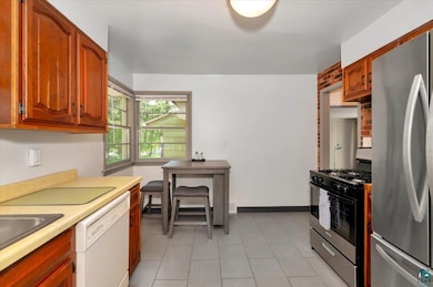 Kitchen with freestanding refrigerator, range with gas stovetop, white dishwasher, light countertops, and brown cabinetry