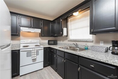 Kitchen featuring a sink, freestanding refrigerator, black microwave, under cabinet range hood, and electric stove