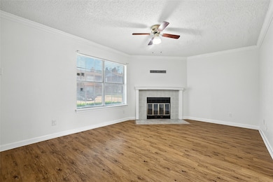Unfurnished living room featuring a textured ceiling, a ceiling fan, a fireplace, wood finished floors, and ornamental molding