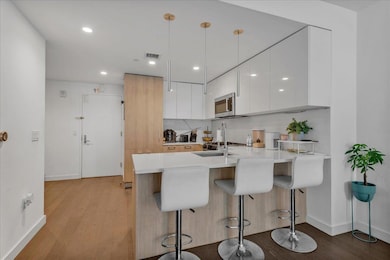 Kitchen with modern cabinets, stainless steel microwave, a peninsula, light wood-style flooring, and a kitchen bar