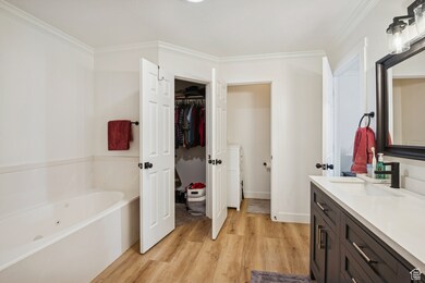 Full bathroom with vanity, light wood-style floors, a garden tub, a walk in closet, and crown molding