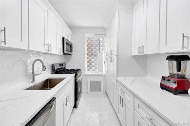 Kitchen with tasteful backsplash, stainless steel appliances, white cabinets, light marble finish flooring, and light stone countertops