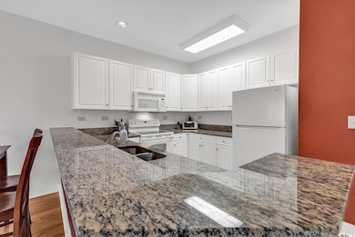 Kitchen with dark stone counters, white appliances, white cabinetry, and light wood-style floors