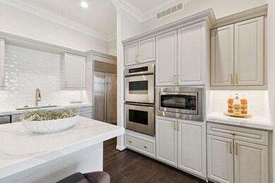 Kitchen with built in appliances, backsplash, light stone counters, dark wood-style flooring, and white cabinets