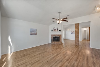 Unfurnished living room with light wood-style flooring, ceiling fan, vaulted ceiling, a fireplace, and a textured ceiling
