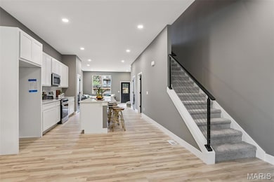 Kitchen with white cabinets, a kitchen breakfast bar, appliances with stainless steel finishes, an island with sink, and light wood finished floors