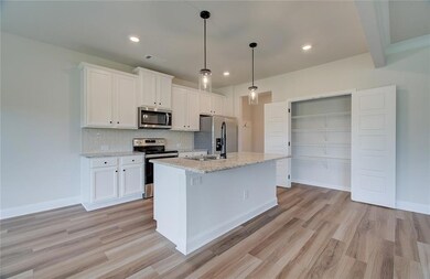 Kitchen featuring appliances with stainless steel finishes, tasteful backsplash, light wood-type flooring, white cabinetry, and an island with sink