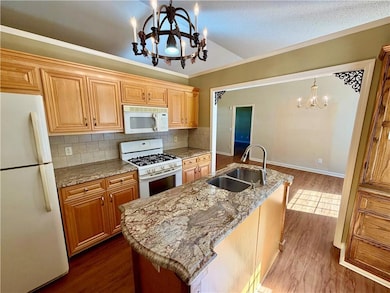 Kitchen with a chandelier, white appliances, backsplash, dark wood finished floors, and pendant lighting