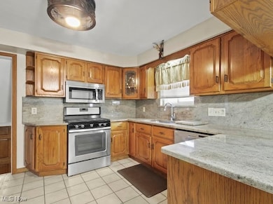 Kitchen with brown cabinetry, decorative backsplash, stainless steel appliances, light tile patterned floors, and light stone counters