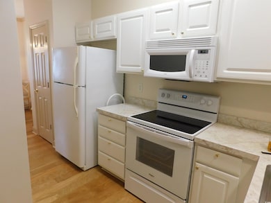 Kitchen with white appliances, light countertops, white cabinets, and light wood-style flooring