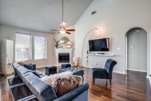 Living room featuring arched walkways, high vaulted ceiling, a fireplace with raised hearth, dark wood-style floors, and ceiling fan