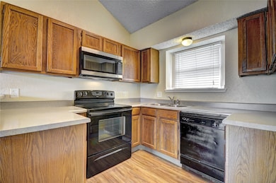 Kitchen with black appliances, light wood finished floors, a textured ceiling, light countertops, and vaulted ceiling