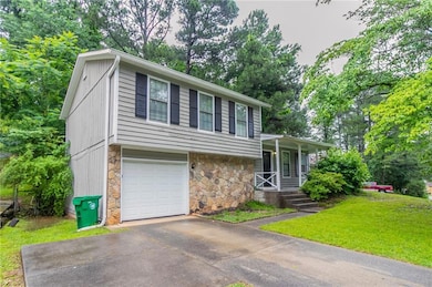 Tri-level home featuring stone siding, covered porch, an attached garage, a front lawn, and concrete driveway