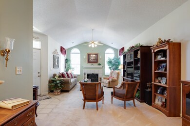 Living room featuring a fireplace, a ceiling fan, lofted ceiling, light carpet, and a textured ceiling