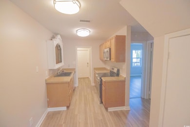 Kitchen with stainless steel appliances, a sink, light wood finished floors, light countertops, and baseboards