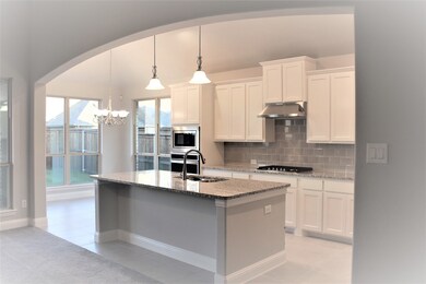 Kitchen featuring decorative backsplash, arched walkways, light stone countertops, hanging light fixtures, and white cabinets