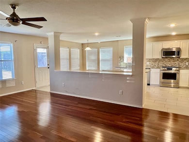 Unfurnished living room featuring cherrywood flooring, ornate columns, and ceiling fan
