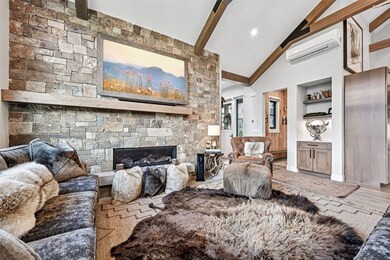 Living room featuring wood finished floors, a wall mounted AC, a stone fireplace, high vaulted ceiling, and beamed ceiling