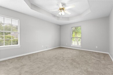 Spare room featuring carpet floors, baseboards, ceiling fan, and a tray ceiling