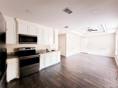 Kitchen with stainless steel appliances, a raised ceiling, white cabinets, and light stone counters