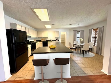 Kitchen featuring black appliances, dark countertops, a textured ceiling, a breakfast bar area, and light tile patterned flooring